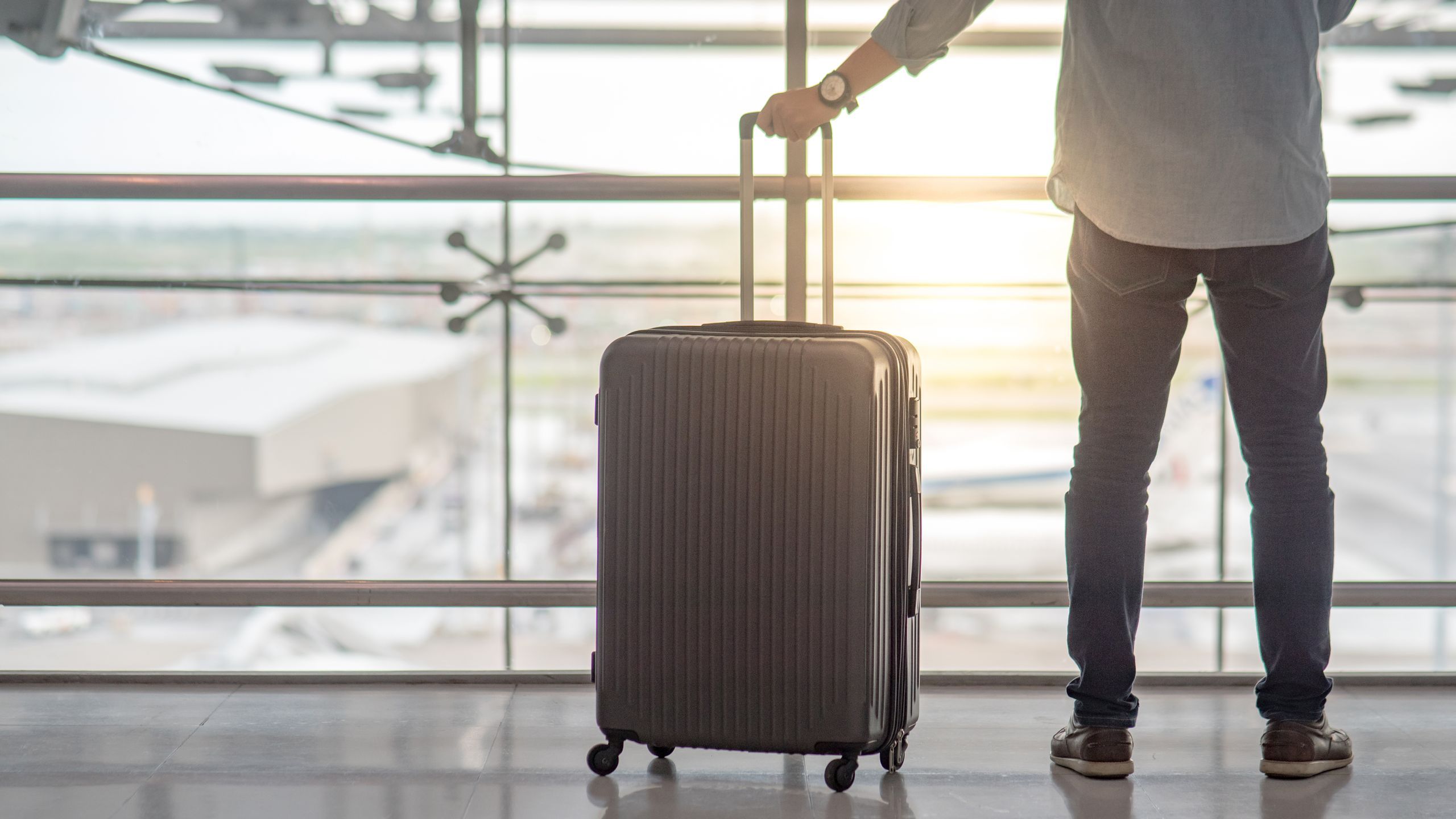 Чемодан в руке человека на фоне аэропорта